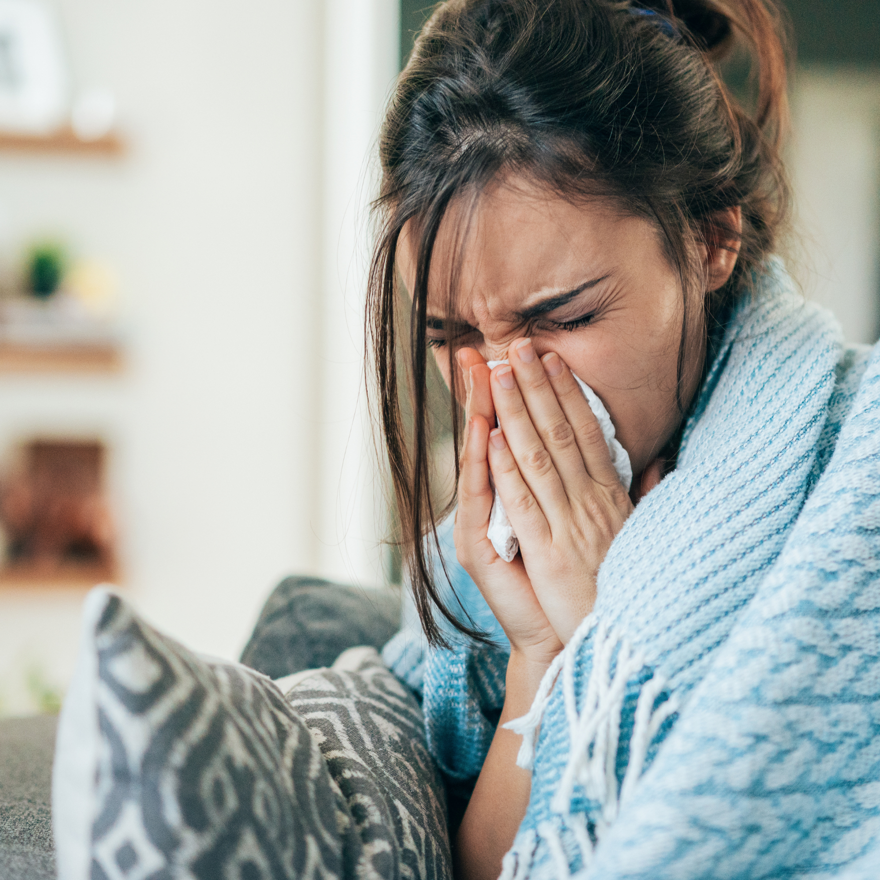 Poorly woman wrapped in blanket sneezing